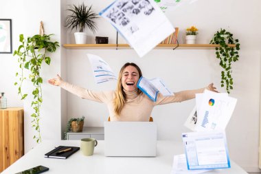 Genç, yetişkin iş kadını kağıtları mutlulukla havaya fırlatıyor. Masada başarısını kutlayan heyecanlı bir serbest yazar. Özgürlük ve motivasyon kavramı.