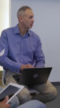 Orta yaşlı iş adamının proje fikirleri toplamak için beyin fırtınası yaptığı dikey HD video. Kendine güvenen lider, modern bir ofiste yaratıcı tartışmalarda iş arkadaşlarına rehberlik ediyor.