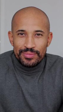 Dikey HD video. Evdeki koltukta oturmuş kameraya bakıp gülümseyen kendine güvenen bir adamın portresi. Odaklanma, kararlılık ve yaşam tarzı kavramı.