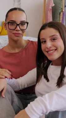 Yatak odasında birlikte oturan iki yetişkin kadının dikey HD videosu. Mutlu Gen Z kadınlarının portresi evde rahatlıyor ve bağ kuruyor. Arkadaşlık ve yaşam tarzı kavramı. 