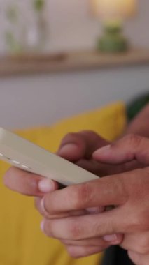 Evdeki bir kanepede oturmuş sosyal medya yayınlarıyla iletişim kuran ve kaydıran akıllı telefonuyla yazı yazan genç bir adamı kapatın. Dikey HD video