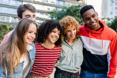 Çok kültürlü bir arkadaş grubu dışarıda eğleniyor. Mutlu genç insanlar yeşil bir kentsel alanda arkadaşlığın ve kahkahanın tadını çıkarıyorlar. Sosyal bağlantı ve yaşam tarzı kavramı.