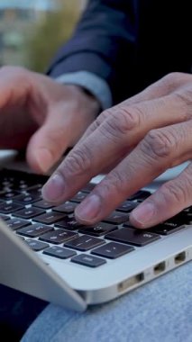 Dışarıda dizüstü bilgisayarda daktilo eden yetişkin bir adamın yakın çekimi. Şehir parkında dijital olarak çalışan bir profesyonel. İş ve teknoloji kavramı.