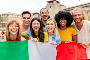İtalyan gençleri gülümsüyor ve ellerinde İtalya bayrağı tutuyorlar. Halk meydanında milli gururlarını ifade eden bir grup arkadaş. Toplum ve kültür kavramı.