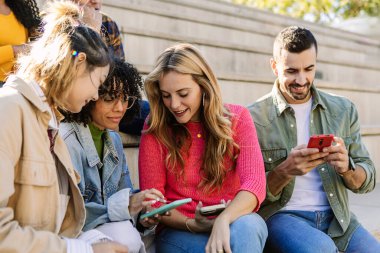 Sosyal medya içeriğini eğlendirirken dışarıda akıllı telefonlar kullanan bir grup genç öğrenci. Arkadaşlık ve yaşam tarzı kavramı.