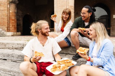 Tarihi İtalyan şehrinde birlikte pizza yiyen bir grup arkadaş. Genç turistler şehir meydanında dışarıda otururken yerel yiyeceklerin tadını çıkarıyorlar. Seyahat ve arkadaşlık kavramı.