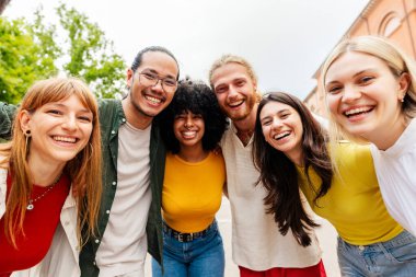 Dışarıda birlikte poz veren çok ırklı bir grup genç arkadaş. Açık bir Avrupa şehrinde sosyal etkileşimden hoşlanan mutlu insanlar. Topluluk ve yaşam tarzı kavramı.