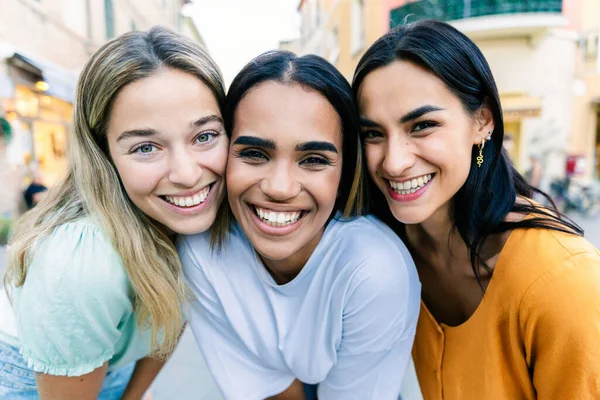 Şehir caddesinde birbirine yakın gülümseyen üç genç kadın. Yakın arkadaşlar yaz tatilinde birlikte vakit geçiriyorlar. Arkadaşlık ve yaşam tarzı kavramı.