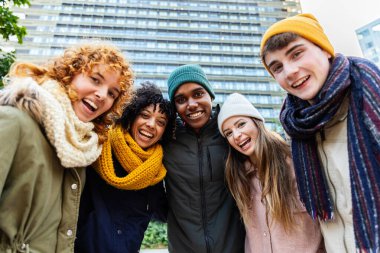 Bir grup mutlu genç arkadaş kışın dışarıda kameraya gülümsüyor. Gençlik toplumu ve arkadaşlık kavramı