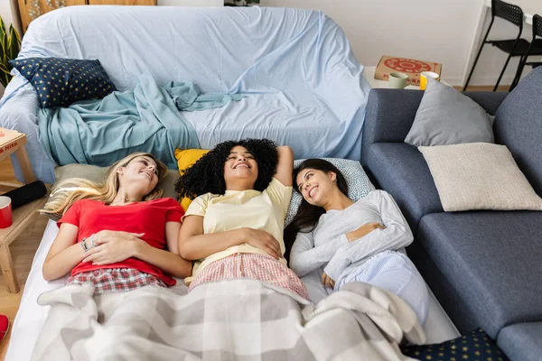 Pijama giyen üç neşeli çok ırklı bayan arkadaş evde pijama partisi sırasında yere uzanıp sohbet ediyorlar. Kadın arkadaşlığı ve gençlik kavramı