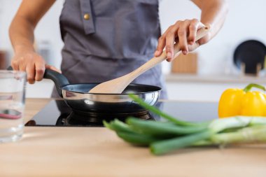 Profesyonel bir aşçı taze sebzelerle yemek hazırlarken tava ve tahta kaşık kullanır.