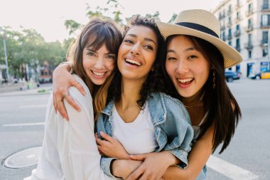 Mutlu bir grup bayan arkadaş dışarıda kucaklaşıyorlar. Çok ırklı genç kadınlar şehirde birlikte vakit geçiriyorlar. Yaşam tarzı ve çeşitlilik kavramı.
