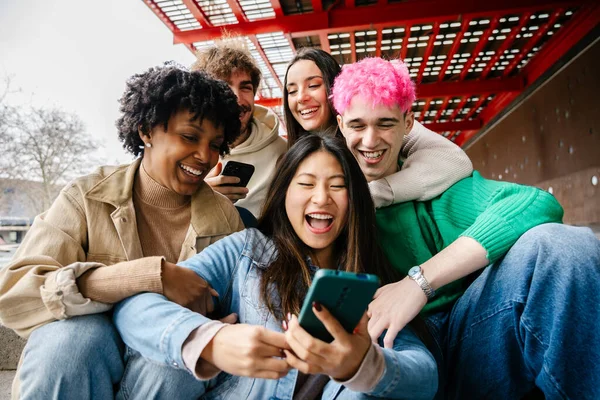Genç bir grup insan dışarıda takılıp cep telefonlarını kullanırken eğleniyor.