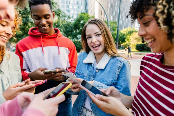 Dışarıda arkadaşlarıyla akıllı telefon kullanan gülümseyen genç bir kadın. Öğrenciler şehir ortamında sosyal medya anlarını paylaşıyorlar. Teknoloji ve yaşam tarzı kavramı.