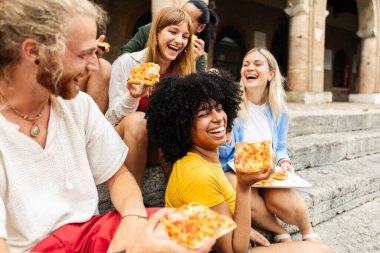 İtalya 'da dışarıda pizza yiyen bir grup çok ırklı arkadaş. Gençler şehir molasında birlikte tatilin tadını çıkarıyorlar. Seyahat ve arkadaşlık kavramı.