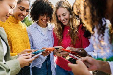Akıllı telefonları kullanan ve dışarıda birlikte gülen bir grup genç kadın. Şehirdeki telefonlarını kontrol ederken gülümseyen çok ırklı bayan arkadaşlar. Sosyal medya ve arkadaşlık kavramı.