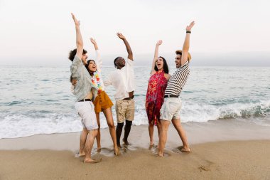 Plajdaki yaz partisinde dans eden mutlu genç arkadaşlar. Çok ırklı insanlar tatilde birlikte eğleniyorlar.