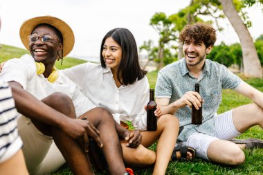 Farklı arkadaş grupları açık havada toplanmaktan zevk alıyor. Şehir parkında çim üzerinde dinlenirken çeşitli genç insanlar biranın tadını çıkarıyor.
