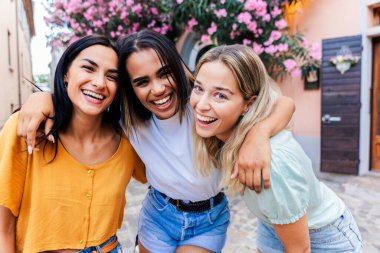 Dışarıda yürüyen ve gülümseyen çok ırklı genç bayan arkadaşlar. Mutlu kadınlar yaz tatili boyunca rahat bir gezintinin tadını çıkarıyorlar. Arkadaşlık ve seyahat kavramı.