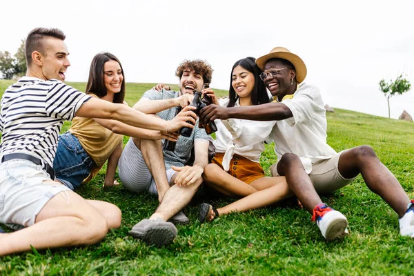 Farklı arkadaş grupları açık havada toplanmaktan zevk alıyor. Şehir parkında çim üzerinde dinlenirken çeşitli genç insanlar biranın tadını çıkarıyor.