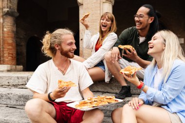 Genç bir arkadaş grubu İtalya gezisi sırasında pizza molası veriyor. Arkadaşlar tarihi şehirde birlikte rahatlıyor ve yerel yemekleri tadıyorlar. Seyahat ve sosyal konsept.