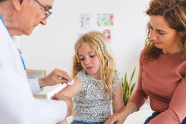 Hastane odasındaki küçük kıza kıdemli erkek doktor aşı yapıyor. Çocuk sağlığı konsepti.