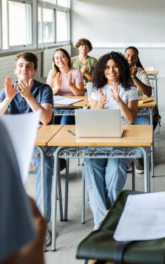 Genç öğrenci grubu ders sırasında alkışlıyor. Lisedeki bir akademik sunumdan sonra çeşitli öğrenciler destek veriyor. Eğitim ve takım çalışması kavramı.
