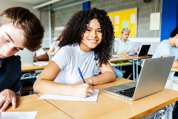 Sınıfta yazan genç kız öğrencinin portresi. Akademik bir lise dersinde not alan gülümseyen bir öğrenci. Eğitim ve gençlik kavramı.