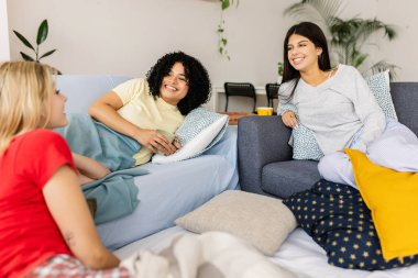 Üç neşeli çok ırklı bayan arkadaş rahat bir pijama partisinin tadını çıkarıyor, rahat koltuklarda sohbet ediyor ve birlikte gülüyorlar. Kadın arkadaşlığı ve gençlik kavramı