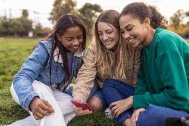 Three diverse young happy student women having fun using mobile phone at college campus. Friendship, technology and youth community concept