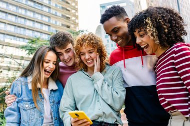 Akıllı telefon içeriğini paylaşan bir grup çok ırklı öğrenci. Öğrenciler dışarıda dijital iletişimle birbirine bağlı. Teknoloji ve sosyal konsept.