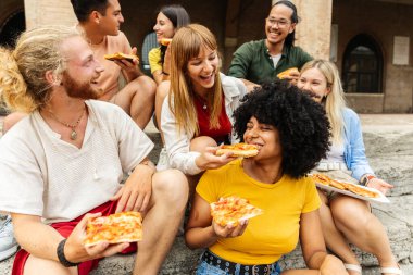 İtalya tatili sırasında pizzayı paylaşan çok ırklı genç arkadaşlar. Birlikte şehir gezisinde yemek ve sohbetin keyfini çıkaran mutlu bir grup. Seyahat ve arkadaşlık kavramı.