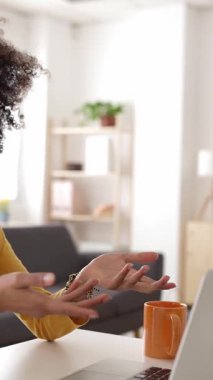 Masasında oturan gülümseyen Afro saçlı Afro-Amerikan kadının videosu. Bilgisayarındaki video konferansında el kol hareketi yapıyor ve konuşuyor. Modern oturma odasından uzaktan çalışıyor.