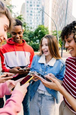Dışarıda telefonları kontrol ederken gülümseyen genç arkadaşlar. Öğrenciler çevrimiçi etkileşimden ve sosyal medyadan birlikte zevk alıyorlar. Teknoloji ve yaşam tarzı kavramı.