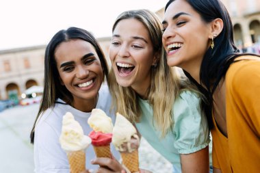 Dondurma yerken birlikte gülen genç kadınlar. Çok ırklı arkadaşlar yurt dışında rahat bir yaz tatilinin tadını çıkarıyorlar. Yaşam tarzı ve seyahat konsepti.
