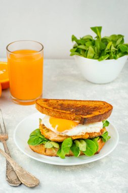 Avrupa kahvaltısı, kızarmış yumurtalı sandviç, tavuk, şifalı otlar ve portakal suyu. Işık masasında kahvaltı, üst manzara. Gıda arkaplanı.