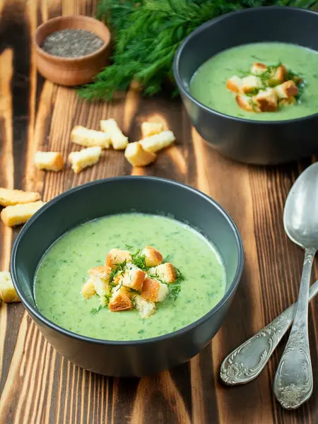 Creamy spinach soup with crackers, herbs and chia seeds. Green soup on a wooden table. Side view.