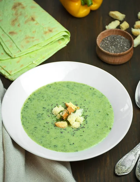 Green zucchini or broccoli cream soup on a wooden table. Green soup. Vegetarian dish. Close-up, flat lay.