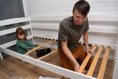 Baba ve küçük kızı bebek yatağını evde bir araya getiriyorlar. Aile takım çalışması