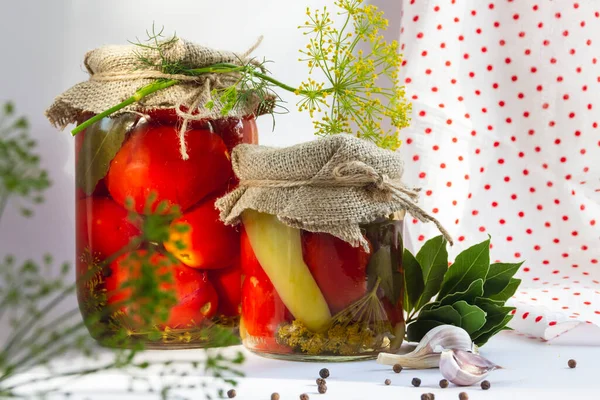 Frascos de vidrio con tomates en escabeche caseros, sellados con tapa metálica sobre fondo amarillo. Pepinos en escabeche, ramitas de eneldo y hojas de laurel. Estilo de país. — Foto de Stock