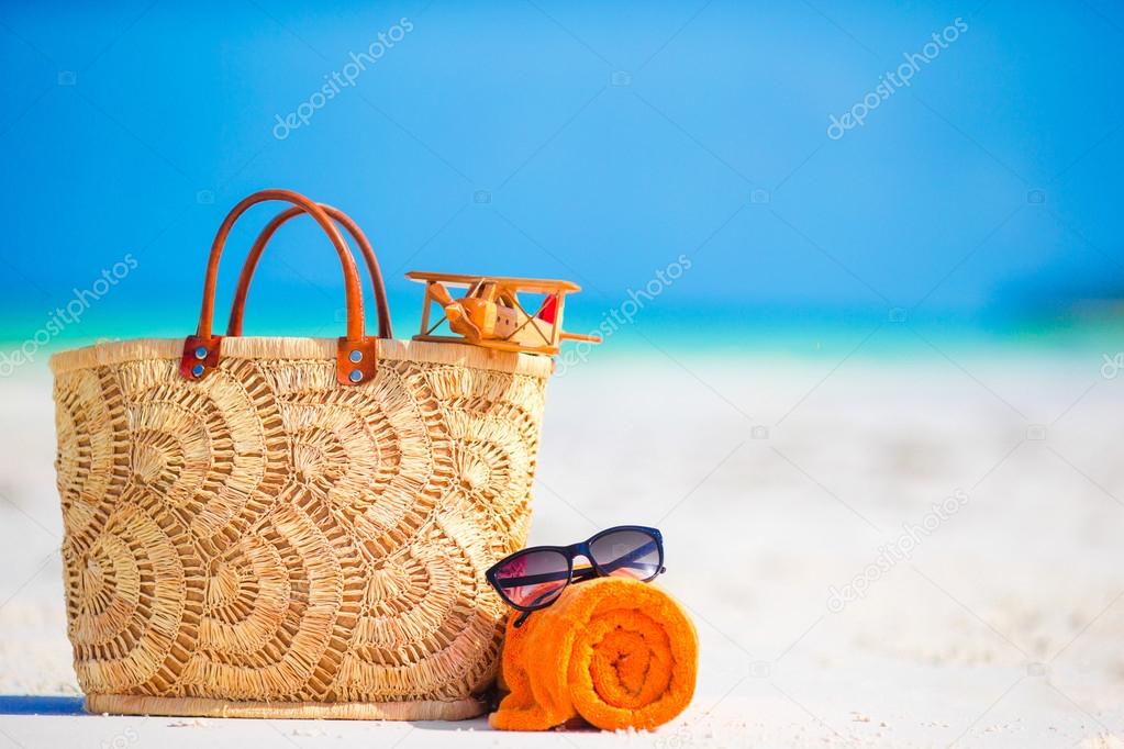 Beach accessories - toy plane, straw bag, orange towel and unglasses on the beach