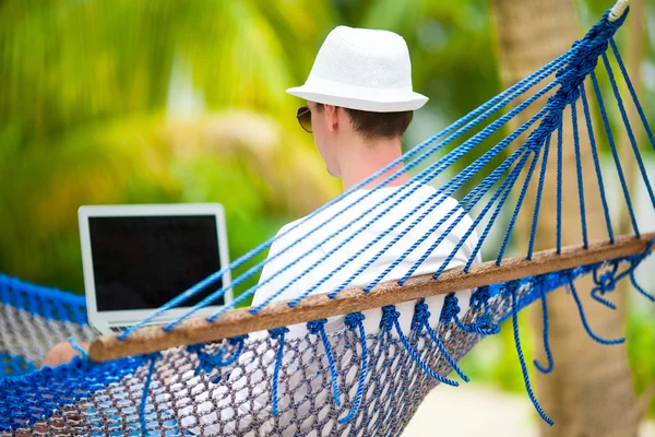 Anak muda dengan laptop di tempat tidur gantung pada liburan tropis — Stok Foto