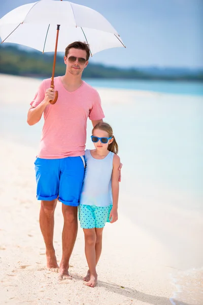 Father and kid at beach with umbrella hiding from sun — Stock Photo, Image