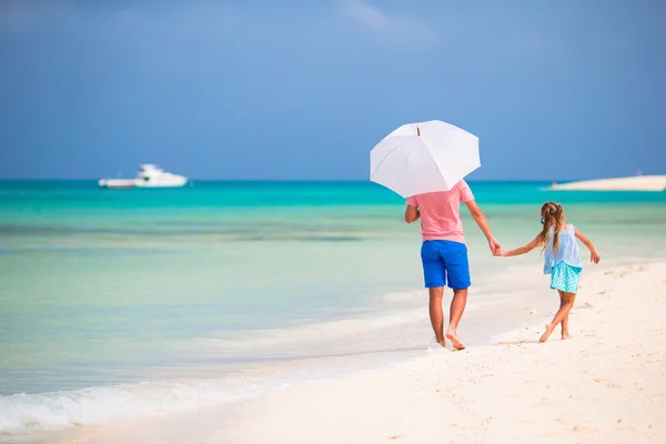 Батько і дочка на пляжі з парасолькою, щоб сховатися від сонця — стокове фото