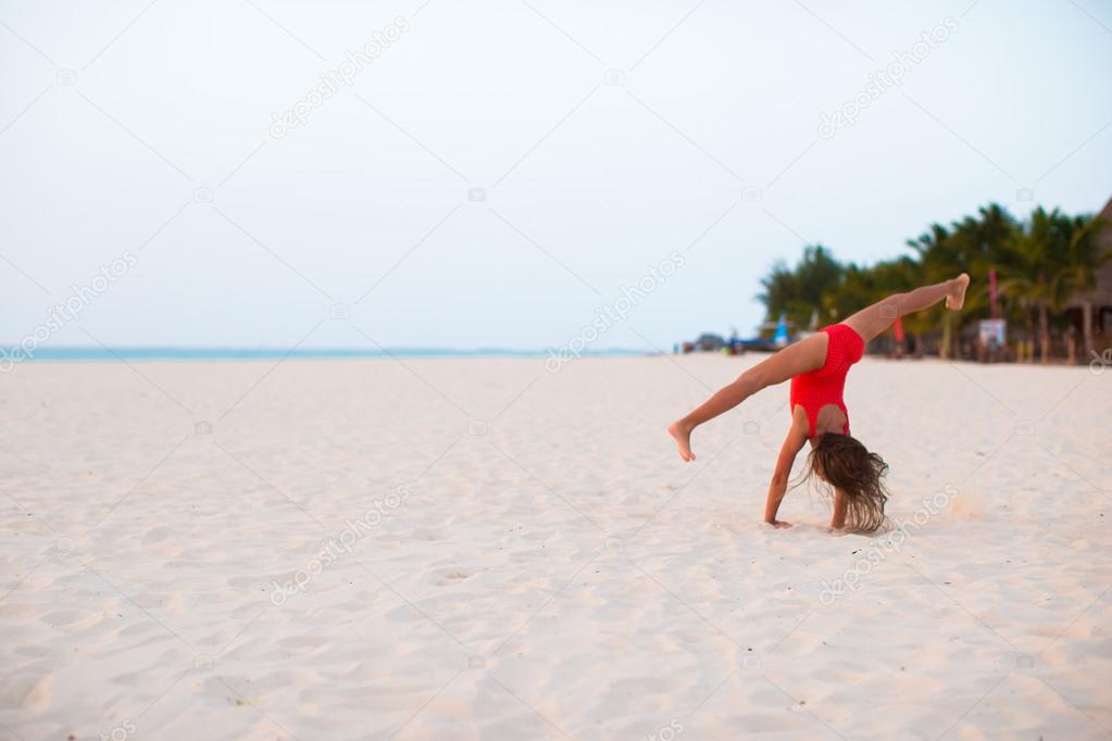 Adorable little girl having fun making cartwheel on tropical white sandy beach