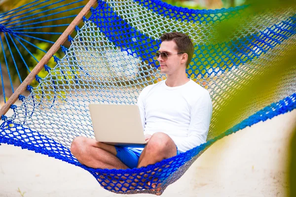 Hombre joven con el ordenador portátil en la hamaca en vacaciones tropicales —  Fotos de Stock