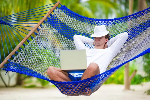 Young man with laptop at hammock on white beach — Stock Photo, Image