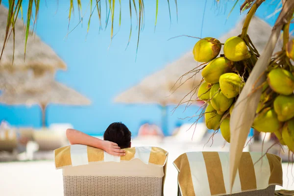 Woman relaxing on sun lounger under a coconut tree — Stock Photo, Image