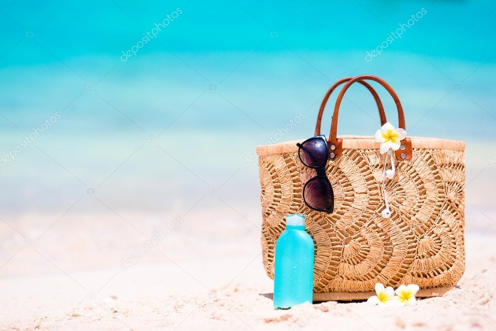 Beach accessories - straw bag, headphones, bottle of cream and sunglasses on the beach