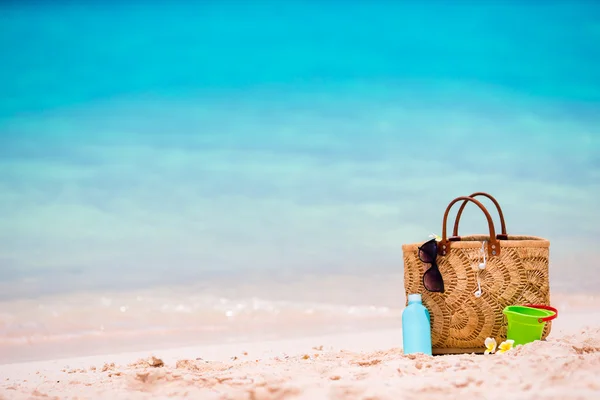 Accesorios de playa - bolsa de paja, botella de crema solar y gafas de sol rojas en la playa —  Fotos de Stock